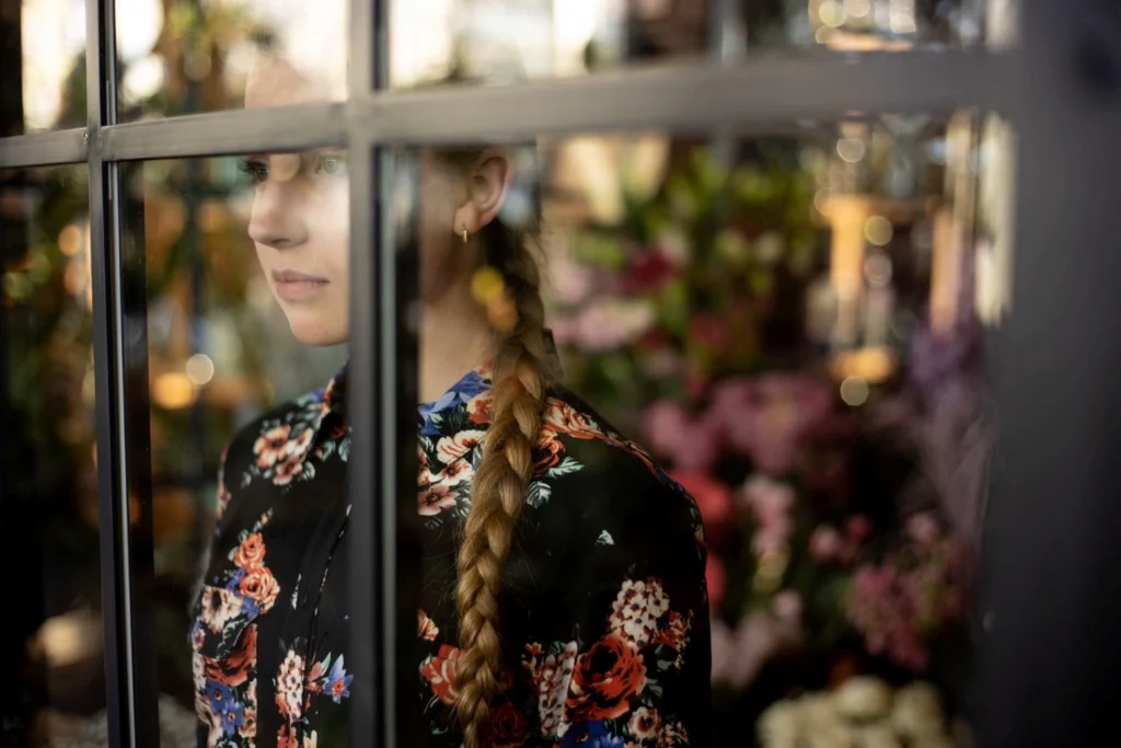 Florystka stojąca w kwiaciarni za szybą wystawową – symbol dystansu między kwiaciarnią a klientem