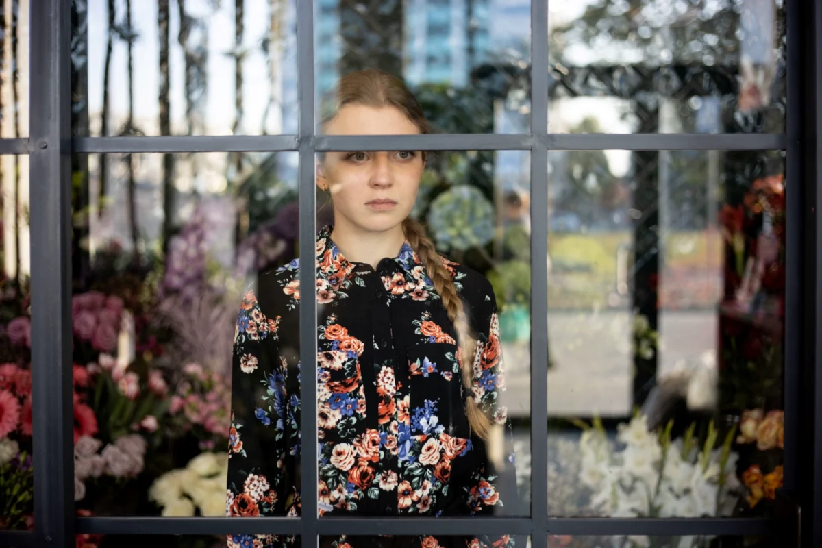 Florystka stojąca w kwiaciarni za szybą wystawową – symbol dystansu między kwiaciarnią a klientem