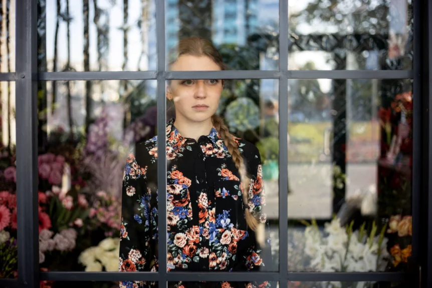 Florystka stojąca w kwiaciarni za szybą wystawową – symbol dystansu między kwiaciarnią a klientem