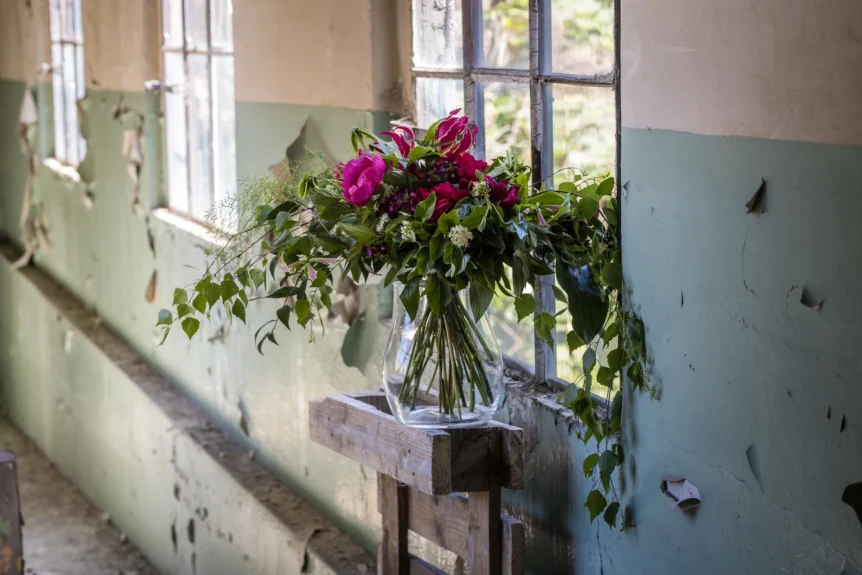 Rozłożysty bukiet z piwoniami i sezonową zielenią w wazonie przy oknie – przykład kompozycji o wyższej wartości niż bukiet za 50 zł