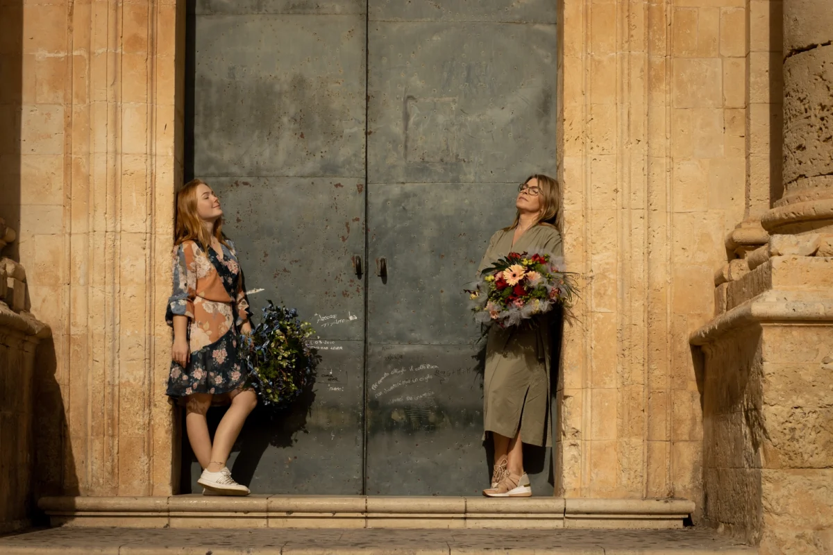 Matka i córka – florystki z bukietami stojące przy dużych drzwiach, symbol współpracy i rodzinnego biznesu