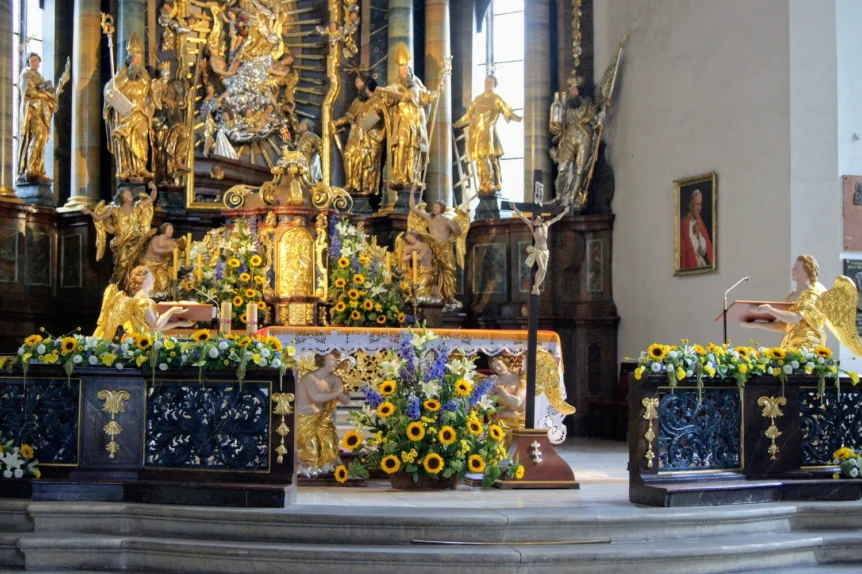 Dekoracja kwiatowa ołtarza w barokowym kościele z kompozycjami ze słoneczników, lilii i kwiatów sezonowych otaczających prezbiterium.