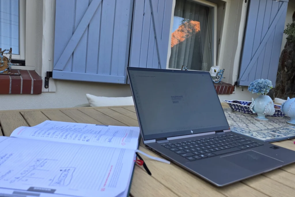 Praca nad Kalendarzem Florysty 2027 – poprzednia edycja z notatkami oraz projekt nowego Kalendarza na ekranie laptopa